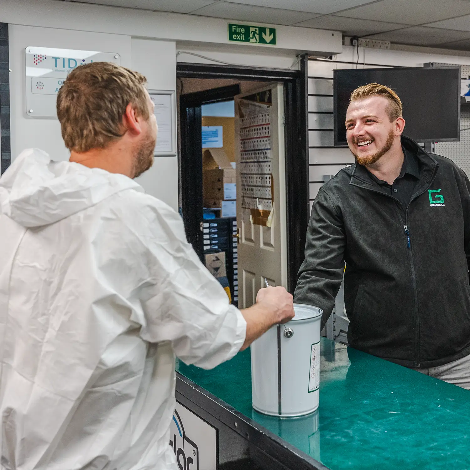 Granville Supplies showroom employee smiling while handing a paint tin to a customer