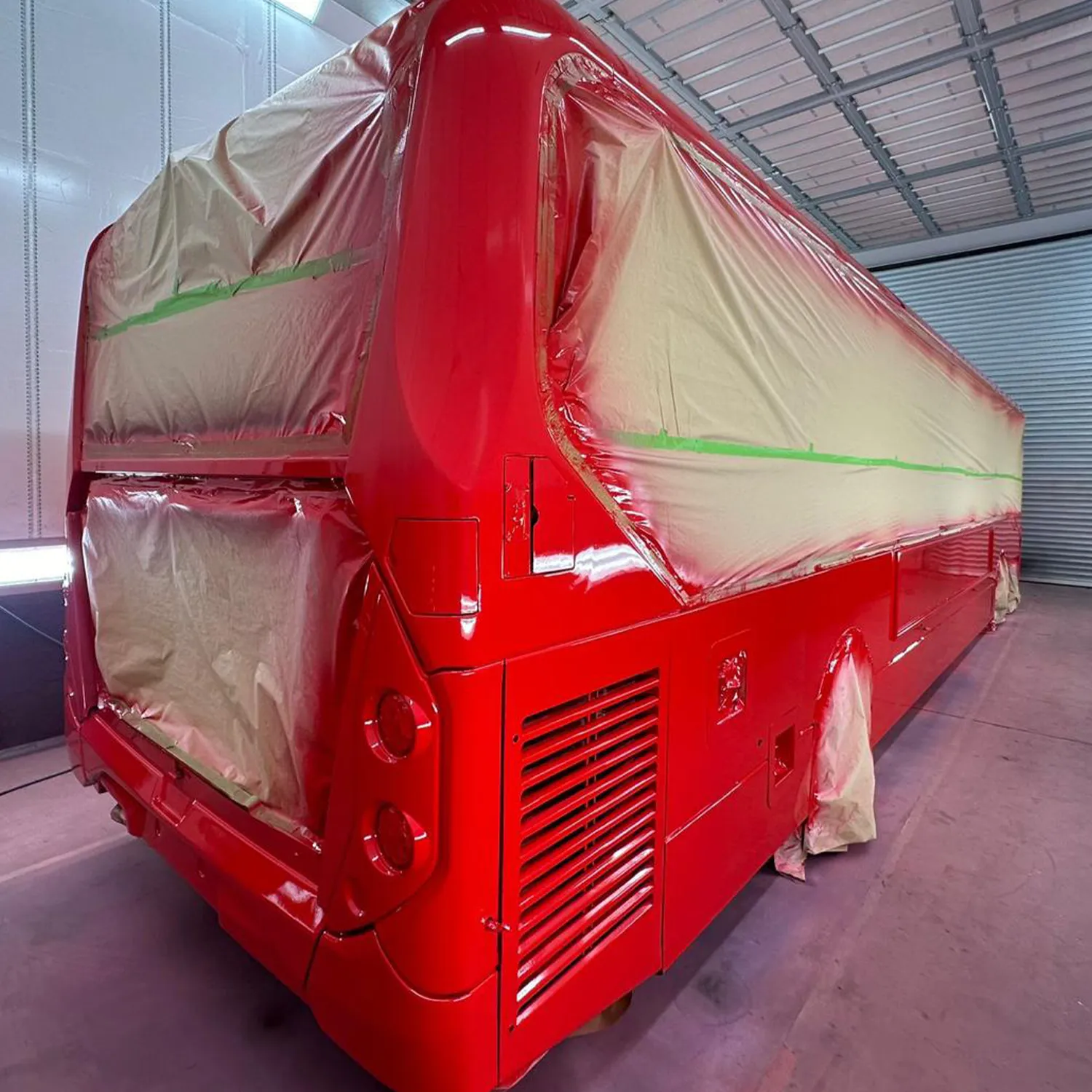 Bus masked inside a spray booth while being painted red during refinishing work
