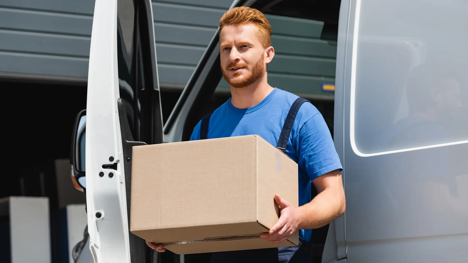 Delivery driver stepping out of a white van while carrying a cardboard box