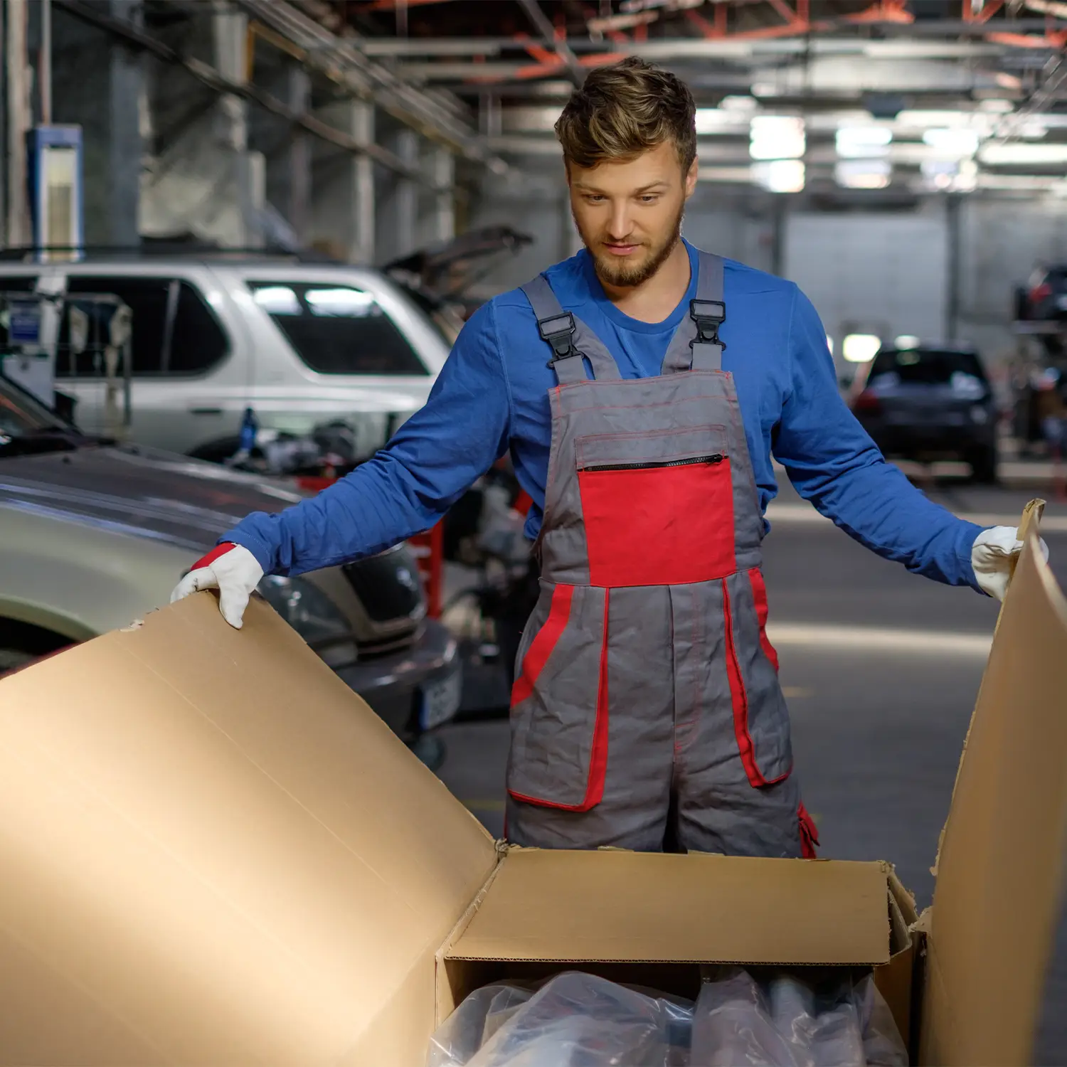 Bodyshop worker unpacking a large box of products with multiple vehicles behind