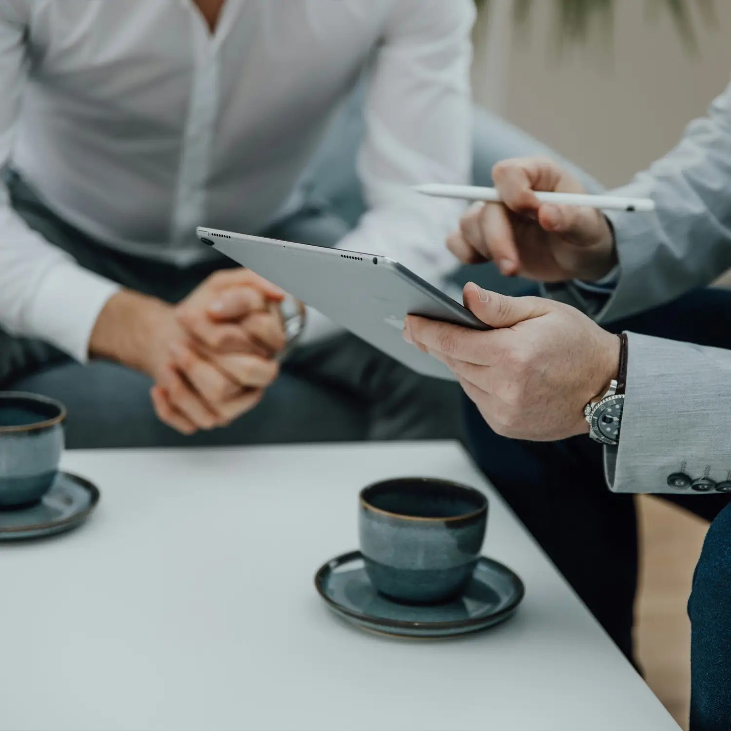 Two men seated at a table discussing information on a tablet over coffee